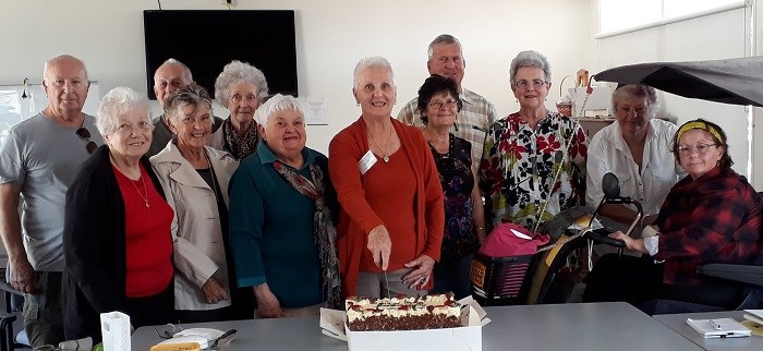 Twelve members of the Bundaberg Stroke Support Group, with one of them cutting a cake